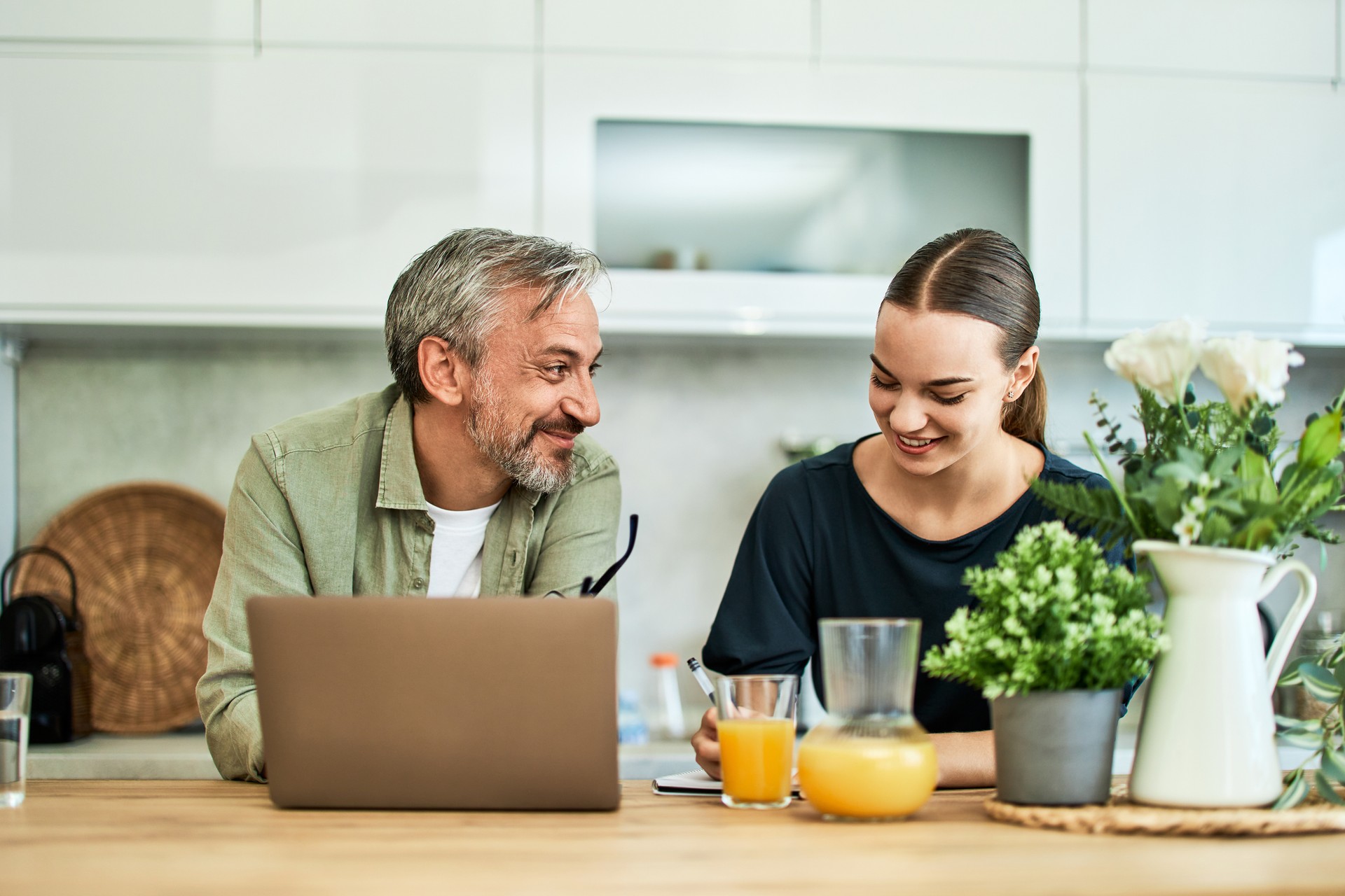 Happy father and daughter using a laptop, leaning on a kitchen island.